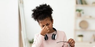 Do You Need Blue Light Glasses? girl-massaging-tired-eyes-sitting-at-desk-at-home
