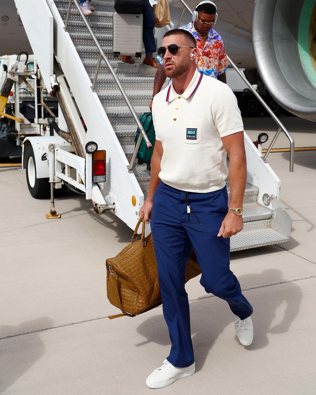 Travis Kelce wearing a white polo and a pair of sunglasses.