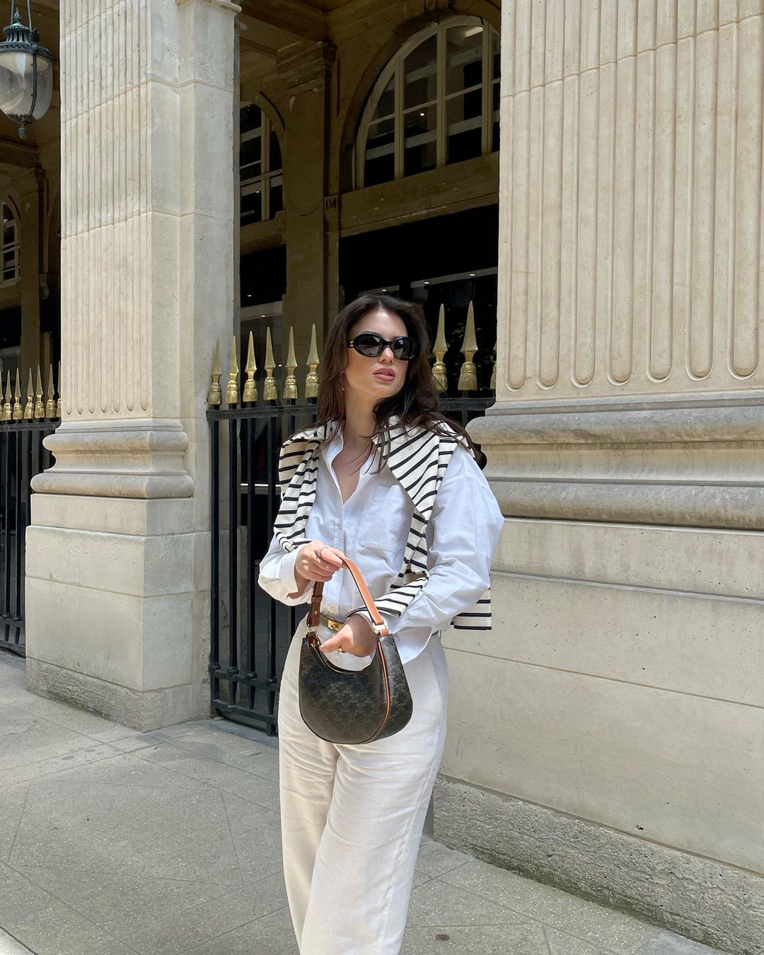 A woman wearing whites and stripes and old-money-inspired sunglasses.