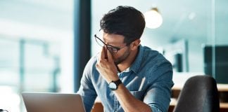 5 Signs Your Eyeglass Frames Are Holding Back Your Productivity in 2026 Man wearing glasses rubs the bridge of his nose while looking at a laptop, showing eye strain during screen time.