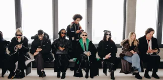 Berlin Fashion Week 2026 Recap: Style & Glasses That Stole the Spotlight A front-row view of Berlin Fashion Week attendees sitting against a bright window, showcasing a mix of oversized black puffer coats, deconstructed leather jackets, and striking geometric eyewear. The aesthetic is cold and industrial, featuring a palette of stark blacks and a single pop of emerald green.