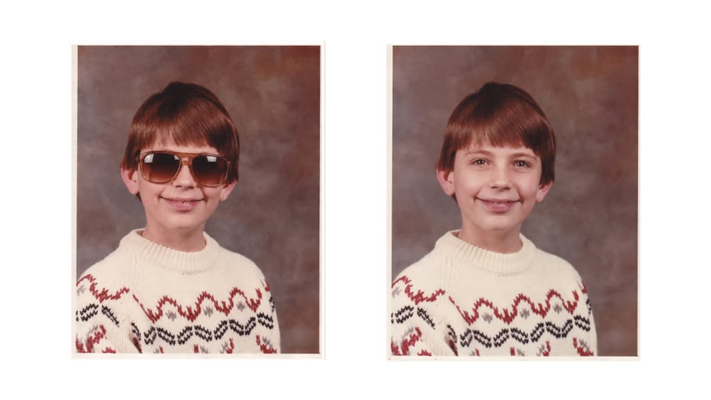 Child's school portrait shown in a side-by-side comparison, with oversized brown aviator-style sunglasses added to the left image and the original portrait without glasses on the right. The child wears a cream knit sweater with a red and black patterned design against a mottled brown studio background.