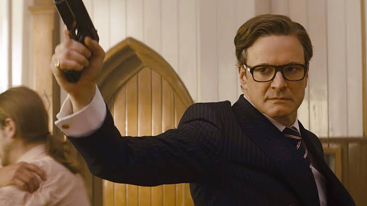 Harry Hart (Galahad) aiming a handgun while wearing rectangular glasses and a dark suit in Kingsman.